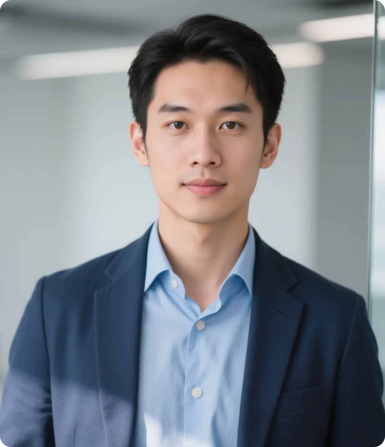 Young Asian man in a blue suit jacket and light blue shirt looking at the camera indoors.