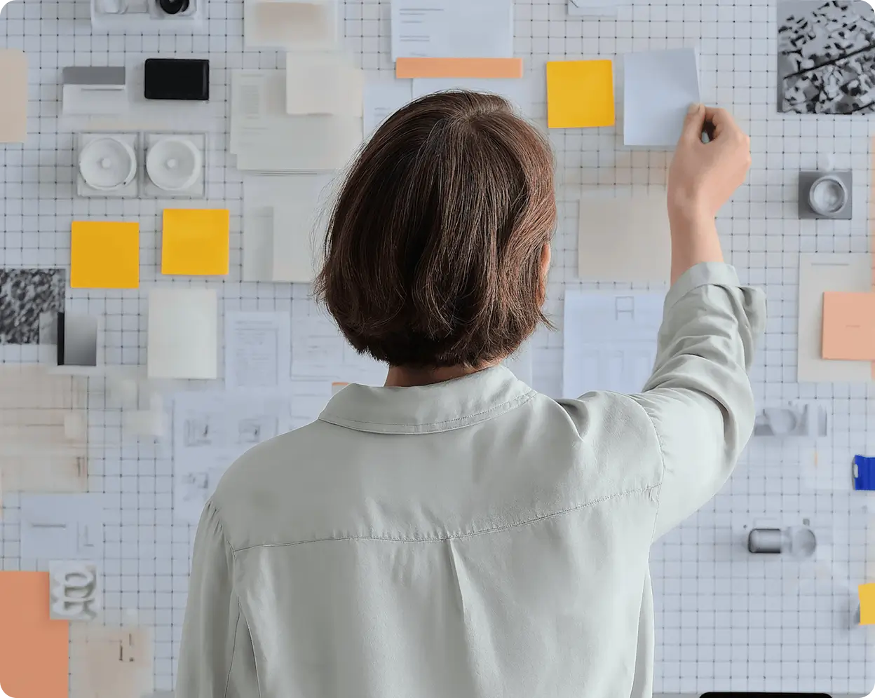 Person arranging colorful sticky notes and papers on a wall with grid lines.