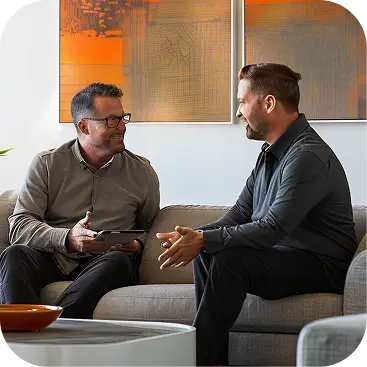 Two men sitting on gray sofas having a conversation in a modern living room with abstract art.