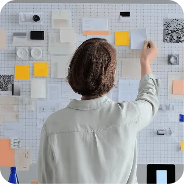 Person viewed from behind arranging notes and papers on a large grid wall.
