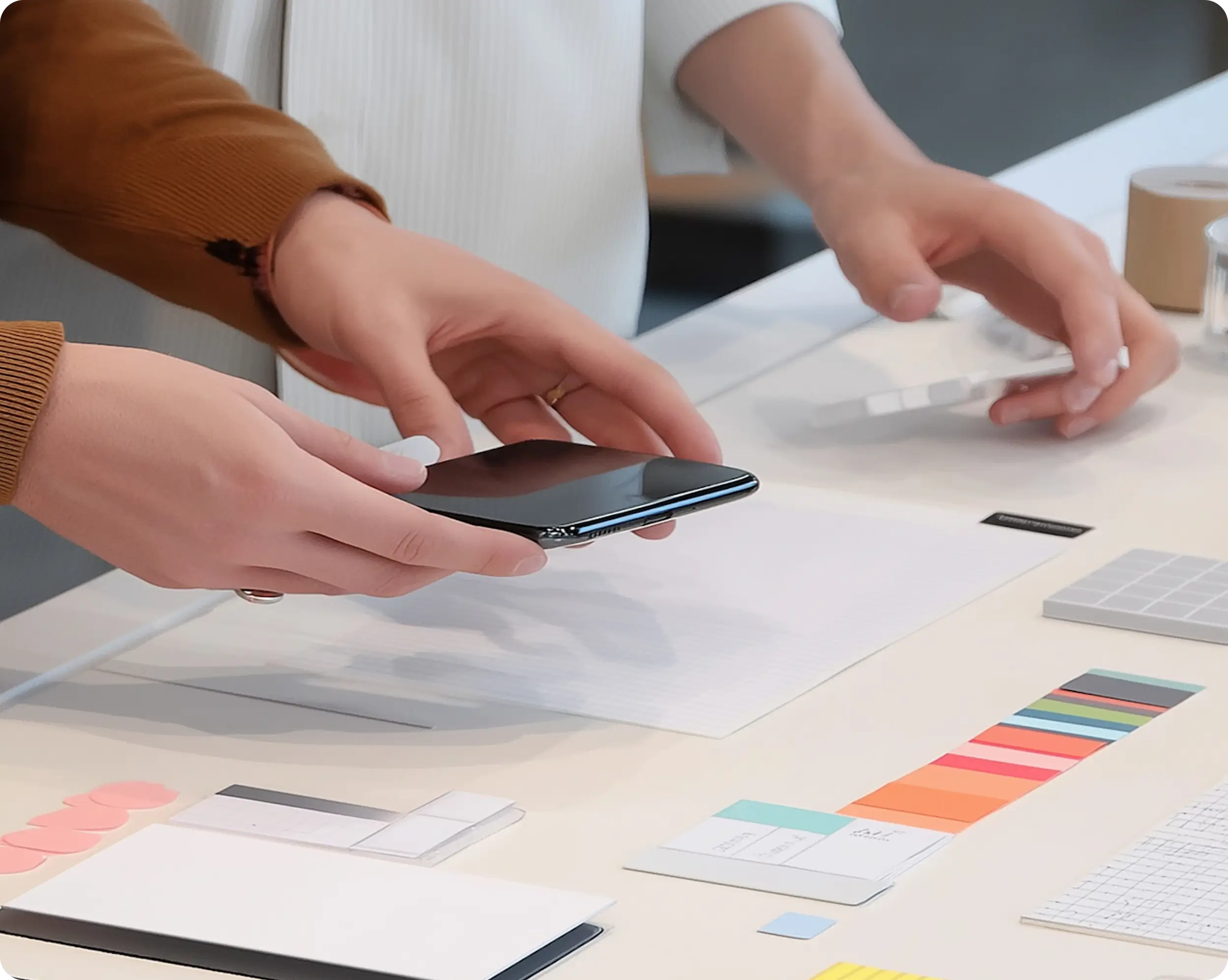 Two people handling a black smartphone over a table with color swatches and paper samples.
